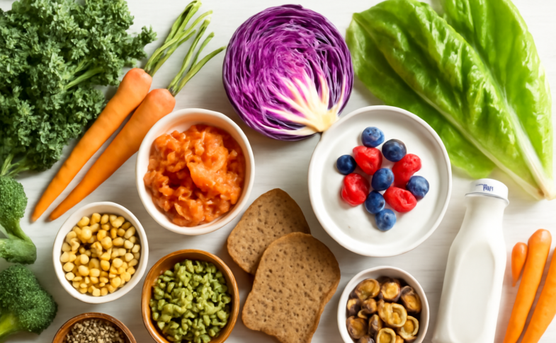 Colorful gut-healthy foods including yogurt, fermented vegetables, fiber-rich plants and whole grains arranged on a white surface